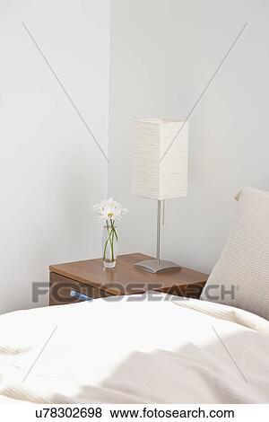Stock Photo - USA, New York, New York City, bed and night table with lamp and daisies in hotel room. Fotosearch