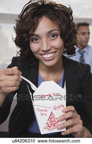 Stock Image - USA, New York, New York City, portrait of smiling young woman eating Chinise food. Fotosearch