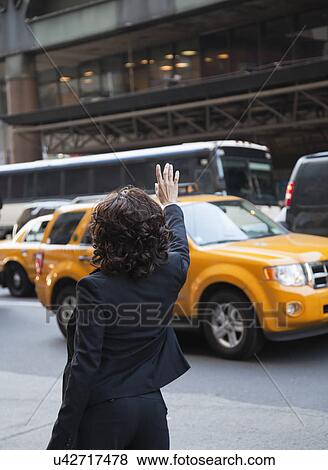 Stock Photo - USA, New York, New York City, rear view of woman hailing taxi. Fotosearch