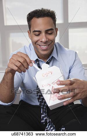 Stock Image - USA, New York, New York City, smiling young man eating Chinise food. Fotosearch