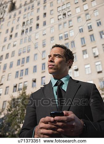 Stock Image - USA, New York, New York City, Businessman with cell phone in front of office building. Fotosearch
