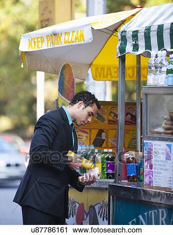 Stock Image - USA, New York, New York City, Businessman at hotdog stand. Fotosearch