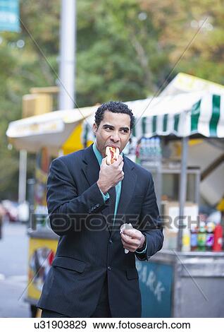 USA, New York, New York City, Businessman eating hotdog on street View Large Photo Image Stock Photo - USA, New York, New York City, Businessman eating hotdog on street. Fotosearch