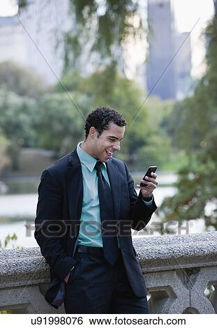 Stock Photograph - USA, New York, New York City Businessman with cell phone in park. Fotosearch