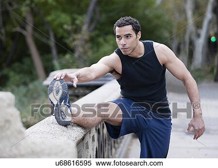 Stock Photography - USA, New York, New York City, Young man stretching legs in park. Fotosearch