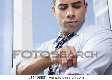 Stock Image - USA, New York State, New York City, business man adjusting shirt by window. Fotosearch