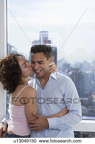 Stock Image - USA, New York State, New York City, young couple embracing by window. Fotosearch