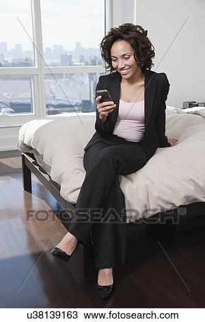 Stock Image - USA, New York State, New York City, business woman using mobile phone on bed. Fotosearch