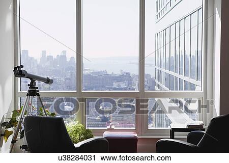 Stock Image - USA, New York State, New York City, Telescope in apartment, New York skyline in background. Fotosearch