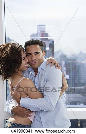 Stock Image - USA, New York State, New York City, young couple embracing by window. Fotosearch