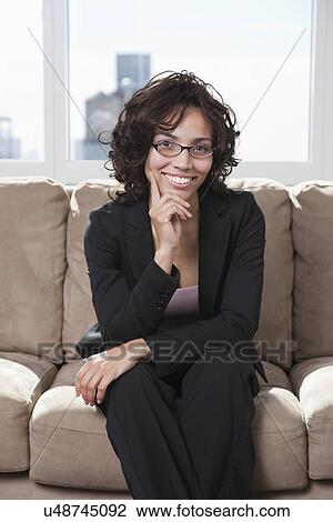 Stock Image - USA, New York State, New York City, portrait of business woman sitting on sofa. Fotosearch