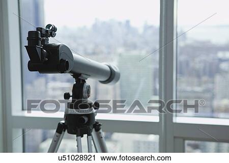 Stock Image - USA, New York State, New York City, Telescope in apartment, New York skyline in background. Fotosearch