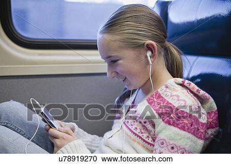 Stock Image - USA, New York State, New York City, Girl (10-11) sitting in train with earphones and listening music . Fotosearch