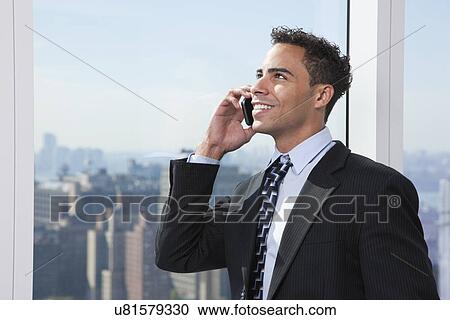 Stock Image - USA, New York State, New York City, business man using mobile phone by window. Fotosearch