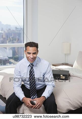 Stock Image - USA, New York State, New York City, portrait of business man sitting on bed. Fotosearch