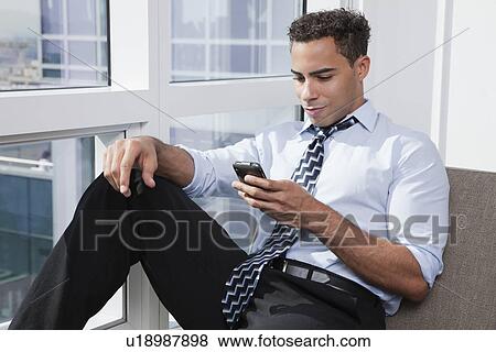Stock Photo - USA, New York State, New York City, business man using mobile phone by window. Fotosearch