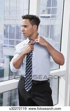 Stock Photo - USA, New York State, New York City, business man adjusting tie by window. Fotosearch