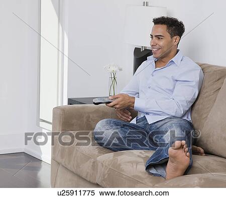 Stock Photography - USA, New York State, New York City, young man watching television on sofa. Fotosearch