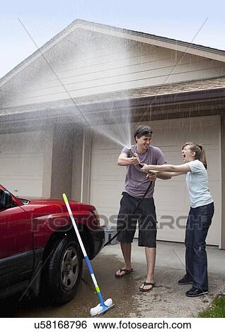 Stock Photograph - USA, Oregon, Ashland, young couple washing car in front of garage. Fotosearch