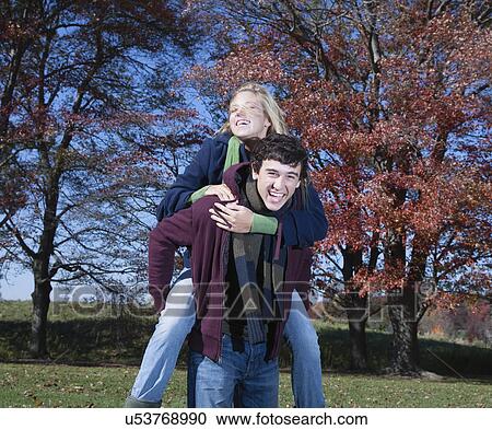 Stock Image - USA, Pennsylvania, Doylestown, teenage boy (16-17) giving piggy back ride to teenage girl in park. Fotosearch