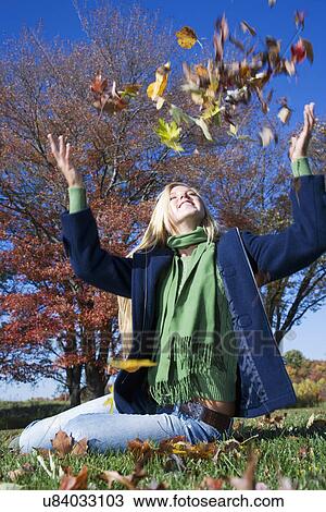 Stock Image - USA, Pennsylvania, Doylestown, teenage girl (16-17) throwing Autumn leaves on lawn in park. Fotosearch