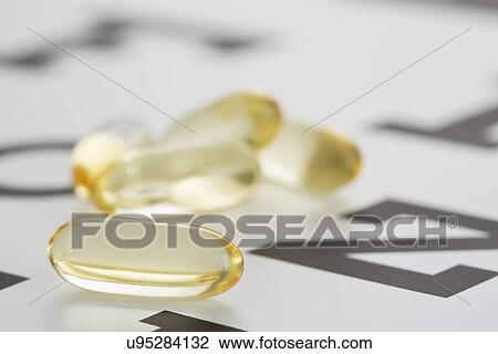 Stock Image - Vitamins, Gel capsules lying on eye chart. Fotosearch