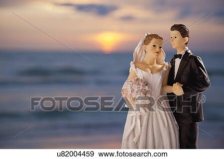 Stock Photo - Wedding figurines on background with sunset over sea, studio shot. Fotosearch