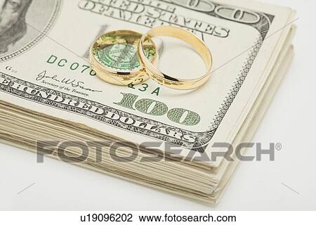 Stock Image - Wedding ring son bunch of dollar banknotes, studio shot. Fotosearch