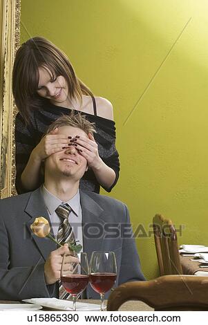 Woman covering man's eyes at restaurant table View Large Photo Image Stock Image - Woman covering man's eyes at restaurant table. Fotosearch