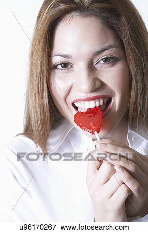 Stock Photo - Woman eating heart shape Valentine's candy, portrait. Fotosearch