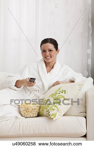 Stock Photo - Woman sitting on sofa and watching tv. Fotosearch