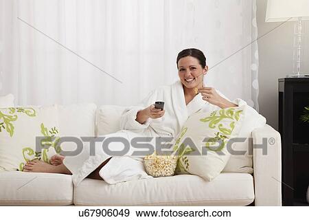 Stock Photo - Woman sitting on sofa and watching tv. Fotosearch