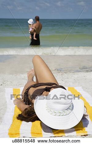 Woman sunbathing on beach, husband with child standing in ocean View Large Photo Image Stock Photo - Woman sunbathing on beach, husband with child standing in ocean. Fotosearch