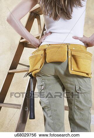 Stock Photograph - Woman wearing tool belt, mid section, rear view. Fotosearch