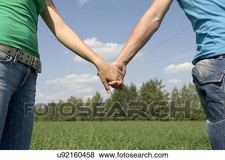 Young couple holding hands on field, mid section View Large Photo Image Stock Photo - Young couple holding hands on field, mid section. Fotosearch