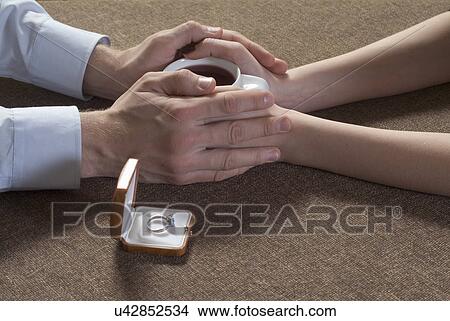 Young couple holding tea cup together beside of engagement ring in box, close-up of hands View Large Photo Image Picture - Young couple holding tea cup together beside of engagement ring in box, close-up of hands. Fotosearch