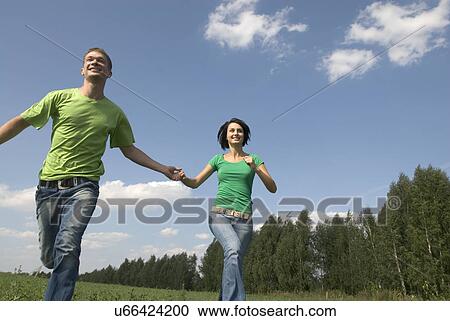 Stock Image - Young couple running trough field. Fotosearch