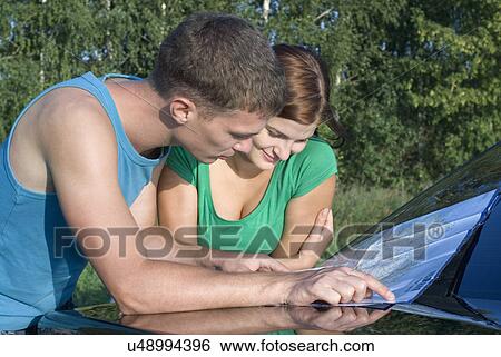 Stock Photograph - Young man and woman reading map on hood of car. Fotosearch