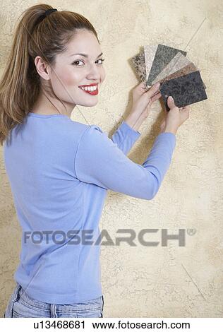 Stock Image - Young woman holding color swatches against wall. Fotosearch