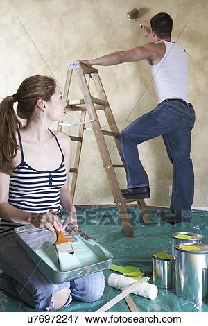 Young woman holding paint tray, man painting wall with roller in background View Large Photo Image Stock Photo - Young woman holding paint tray, man painting wall with roller in background. Fotosearch