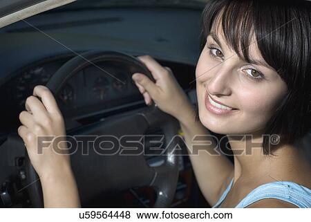 Stock Photo - Young woman sitting in car and holding steering wheel. Fotosearch