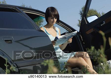 Stock Image - Young woman sitting in car and reading map, mid section. Fotosearch