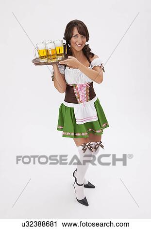 Stock Image - Young woman wearing Oktoberfest costume holding tray with beers, studio shot. Fotosearch