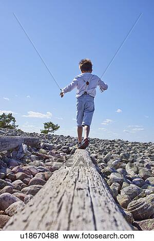 Stock Photo - Boy balancing on log on beach. Fotosearch