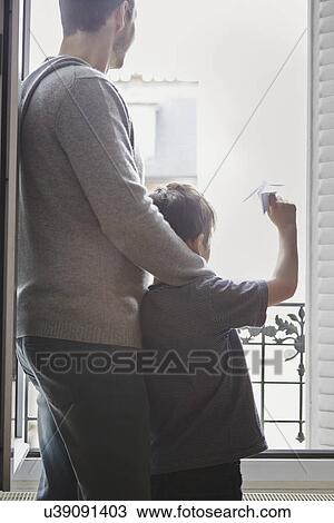 Stock Image - Boy launching paper plane from window. Fotosearch