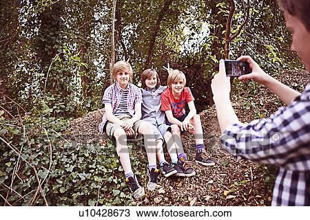 Stock Image - Boy photographing friends with phone in forest. Fotosearch