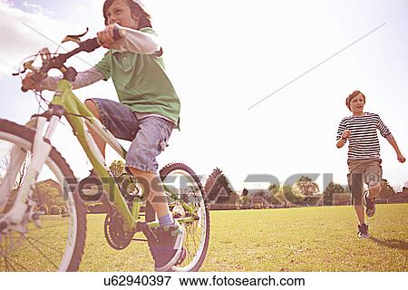 Boys running and cycling on playing field View Large Photo Image Stock Photo - Boys running and cycling on playing field. Fotosearch