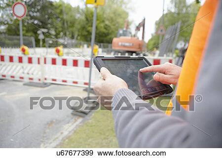 Stock Photo - Close up of foremans hands using digital tablet on road construction site. Fotosearch