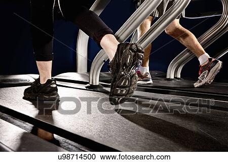 Stock Image - Close up of male and female legs running on gym treadmill in altitude centre. Fotosearch