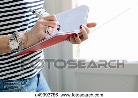 Stock Photograph - Close up of mature woman at home writing in notebook. Fotosearch